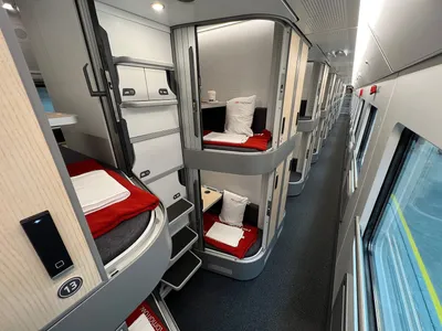 Mini cabins stacked on two levels along the aisle of a new-generation Nightjet car, doors open, each with a made-up single berth.
