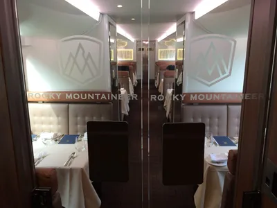 The lower-level dining room of a Rocky Mountaineer GoldLeaf coach in 2016, seen through glass doors, with tables laid for a meal.