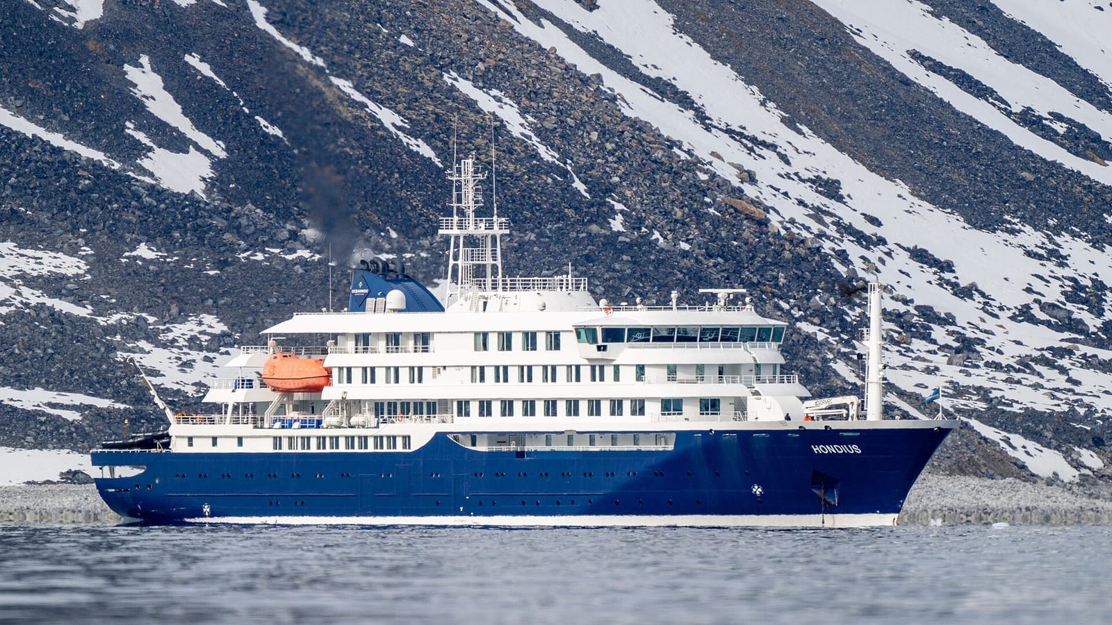The expedition ship Hondius in Magdalenefjorden, Svalbard, in June 2025, in front of a snow-streaked rocky shore.
