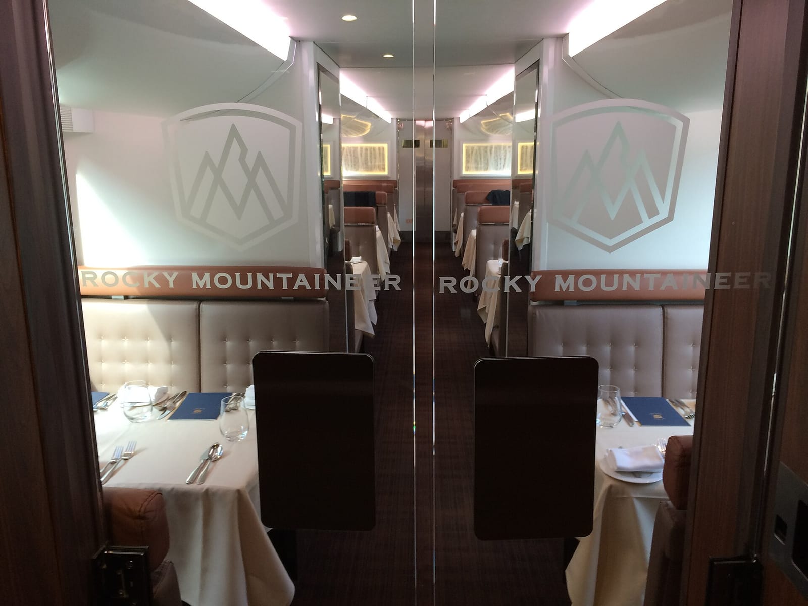 The lower-level dining room of a Rocky Mountaineer GoldLeaf coach in 2016, seen through glass doors, with tables laid for a meal.
